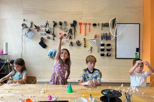 Children engaged in a creative activity at a table with various tools and materials on a pegboard wall.